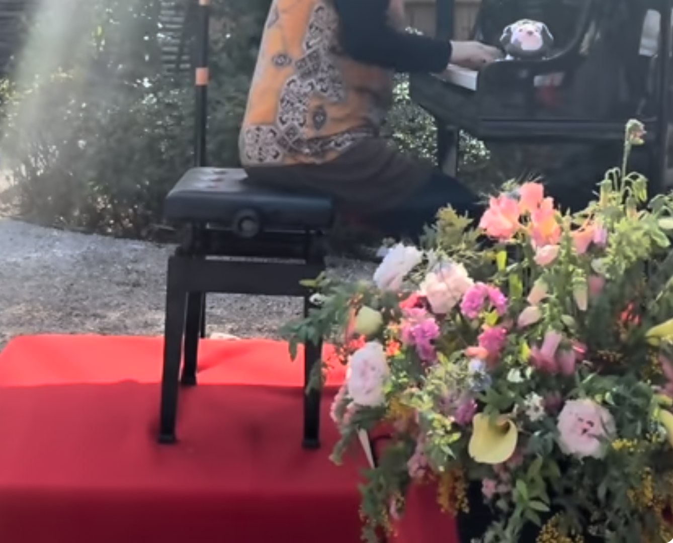 花に囲まれた屋外のグランドピアノで演奏する講師